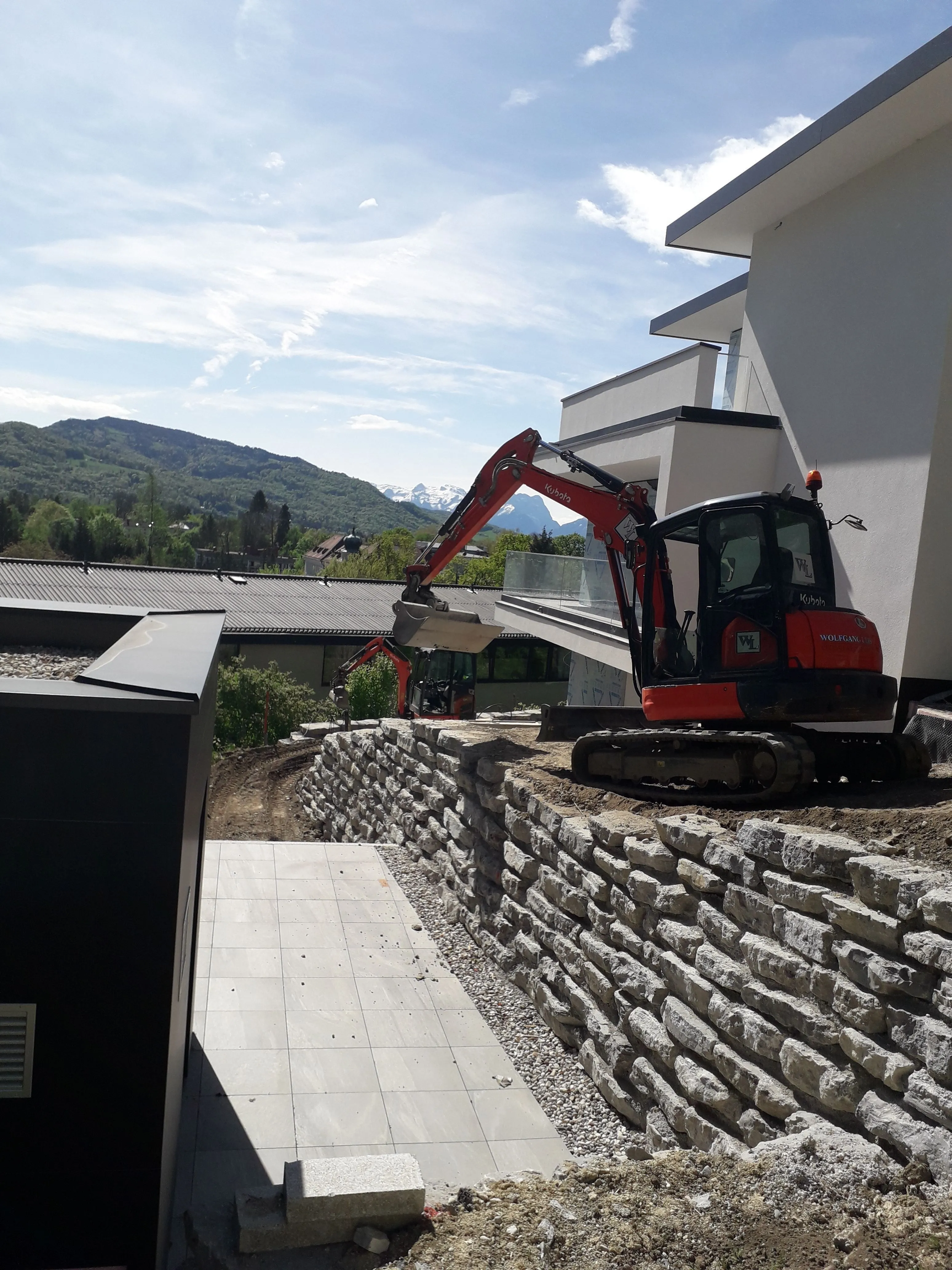 Minibagger beim Schlichten einer Natursteinmauer an einem Neubau